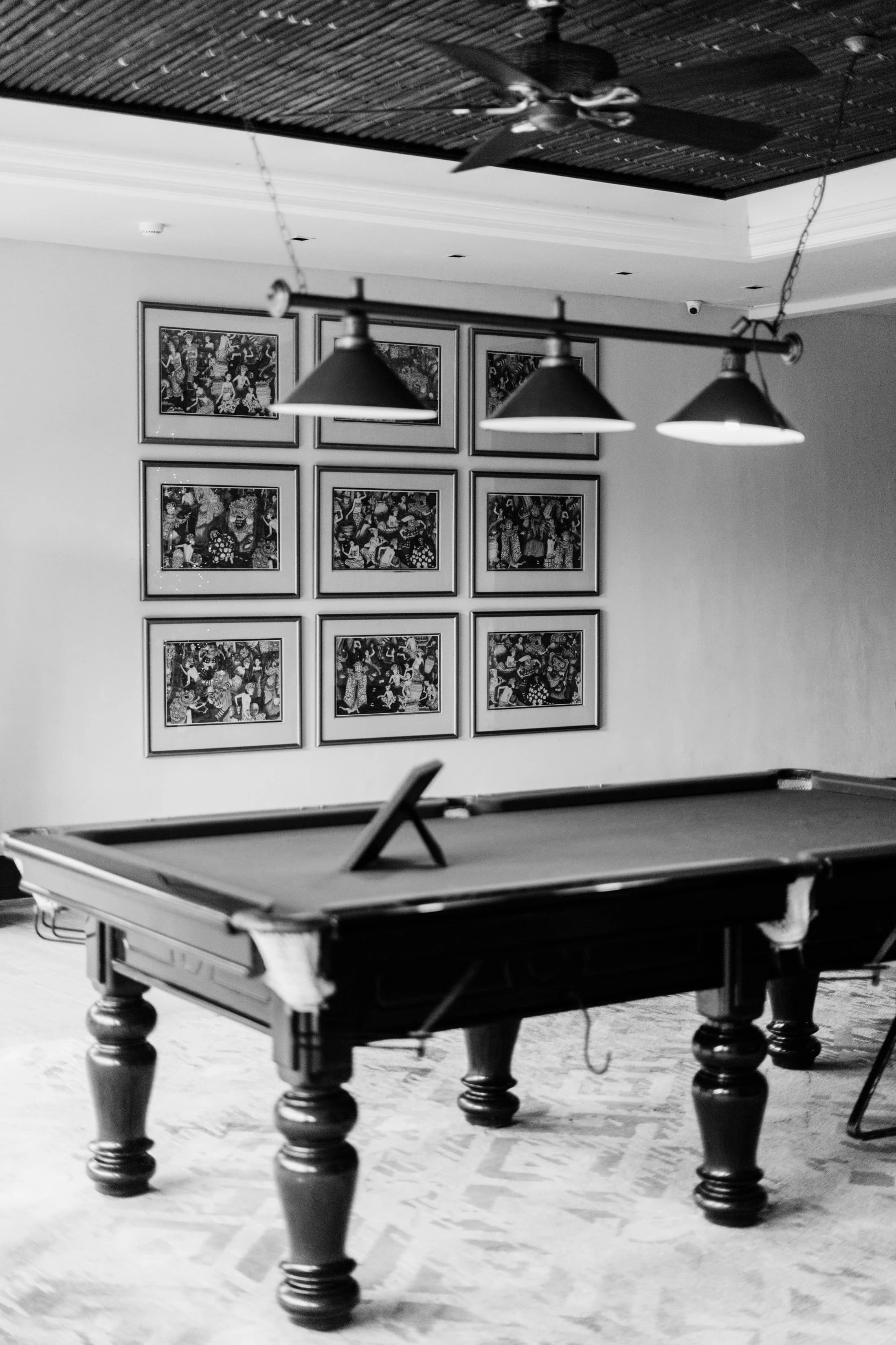 A solid wooden billiards table beneath pendant lamps